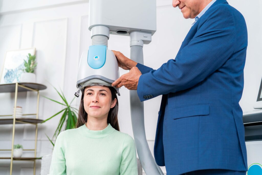 woman in a chair receiving tms treatment by a male emloyee